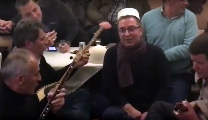 VIDEO/ Deputeti i LSI këmbëkryq në sofër, këndon me rapsodët me qeleshe e çifteli